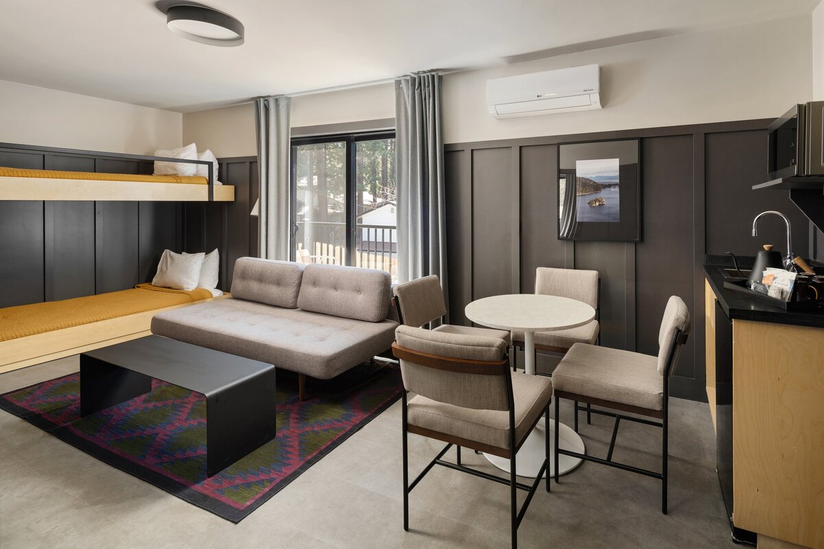 A modern living room with a kitchenette, dining table, sofa, bunk bed, and flat-screen TV.