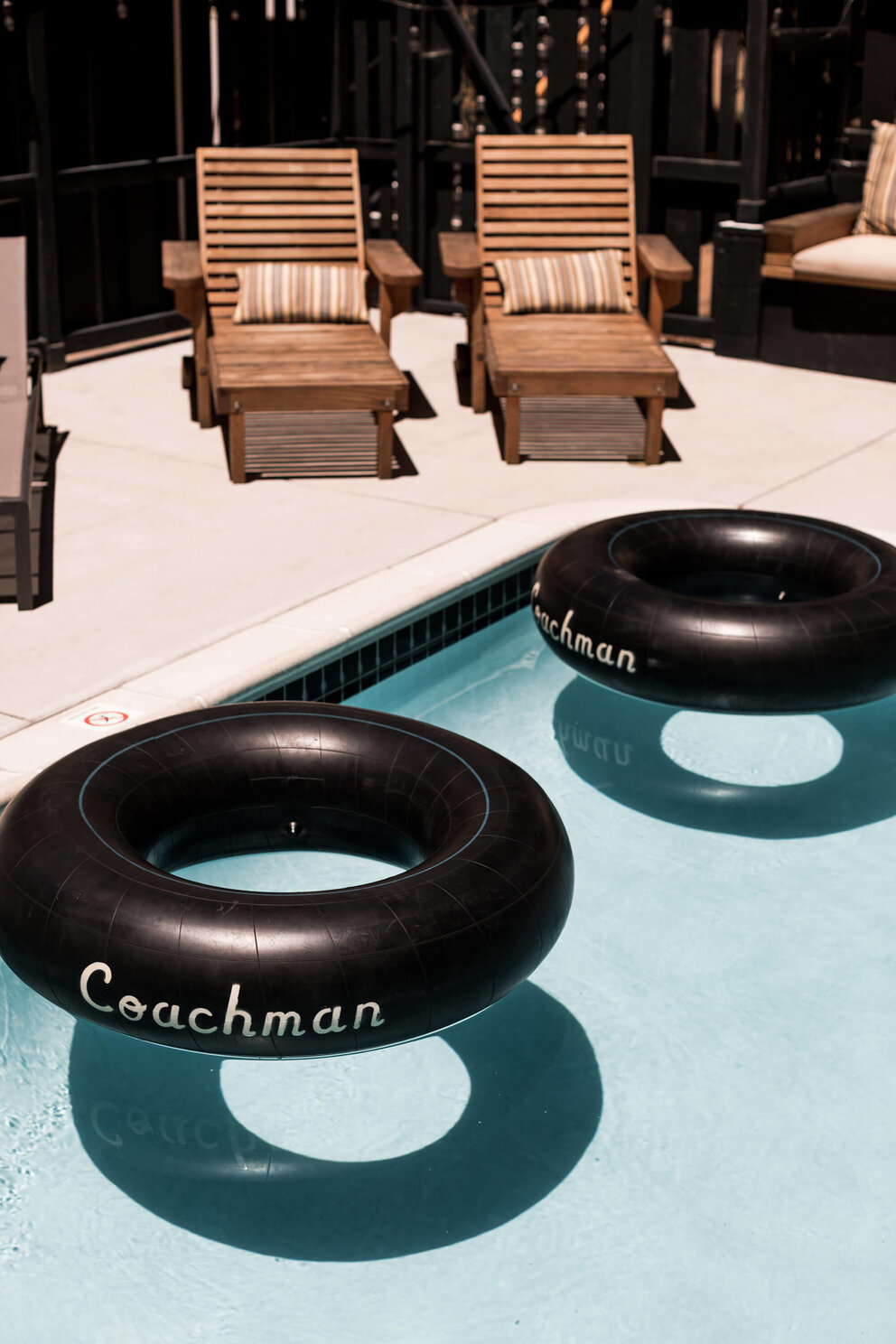 A pool scene with black inflatable tubes and wooden lounge chairs